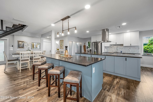 kitchen with dark hardwood / wood-style flooring, pendant lighting, island exhaust hood, a center island, and white cabinetry