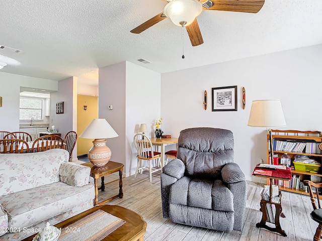 living room featuring a textured ceiling, light hardwood / wood-style flooring, and ceiling fan