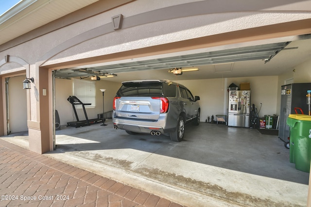 garage with stainless steel refrigerator with ice dispenser, a garage door opener, and refrigerator