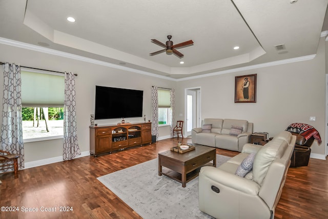 living room with a tray ceiling, dark wood-type flooring, ornamental molding, and ceiling fan