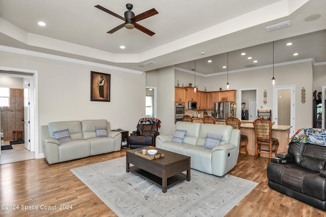 living room featuring light wood-type flooring, ornamental molding, a tray ceiling, and ceiling fan