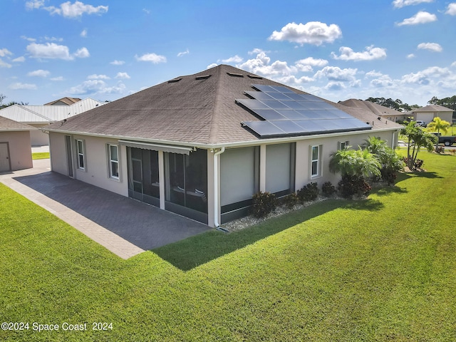 back of house featuring a sunroom, a lawn, and solar panels