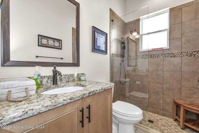 bathroom featuring vanity, toilet, a tile shower, and tile patterned flooring