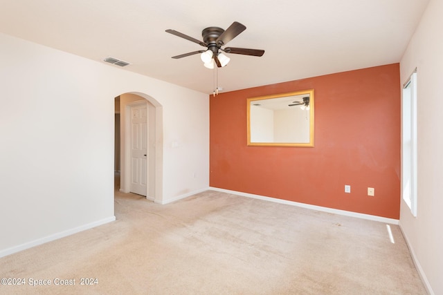 empty room featuring arched walkways, visible vents, a ceiling fan, light carpet, and baseboards