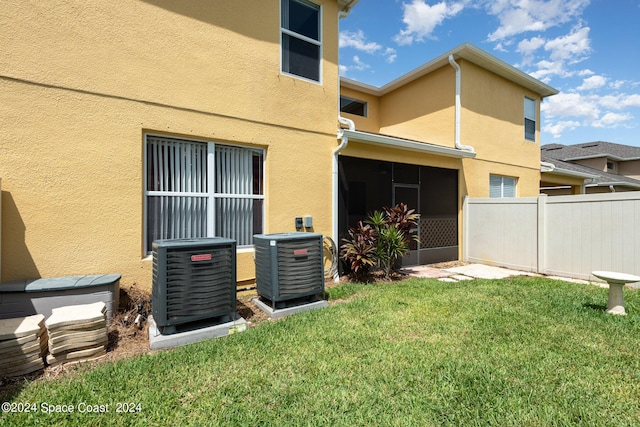 rear view of house featuring stucco siding, a lawn, fence, and central air condition unit