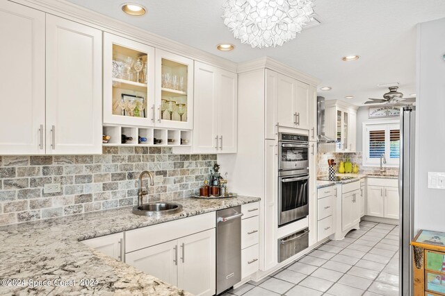 kitchen featuring ceiling fan with notable chandelier, stainless steel double oven, light stone counters, and sink