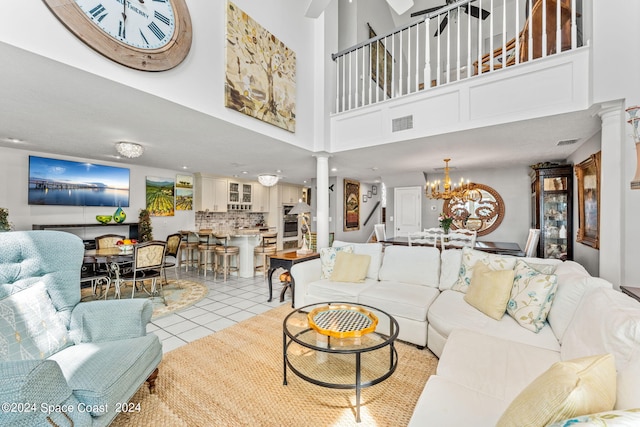 living area featuring a towering ceiling, an inviting chandelier, light tile patterned flooring, ornate columns, and stairs