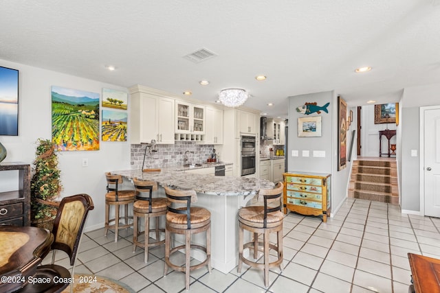 kitchen with visible vents, decorative backsplash, a peninsula, a kitchen bar, and a sink