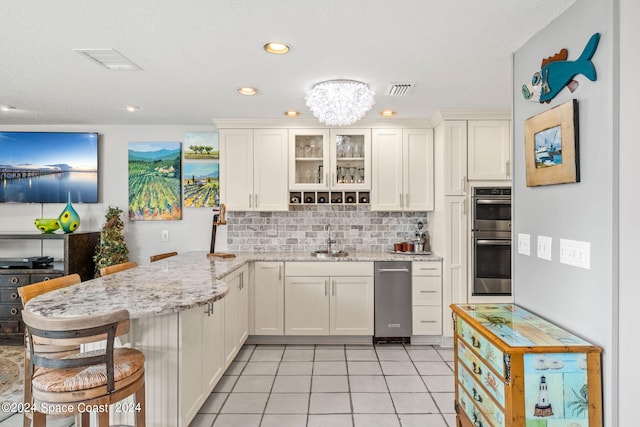 kitchen featuring a breakfast bar area, light stone countertops, kitchen peninsula, sink, and stainless steel double oven