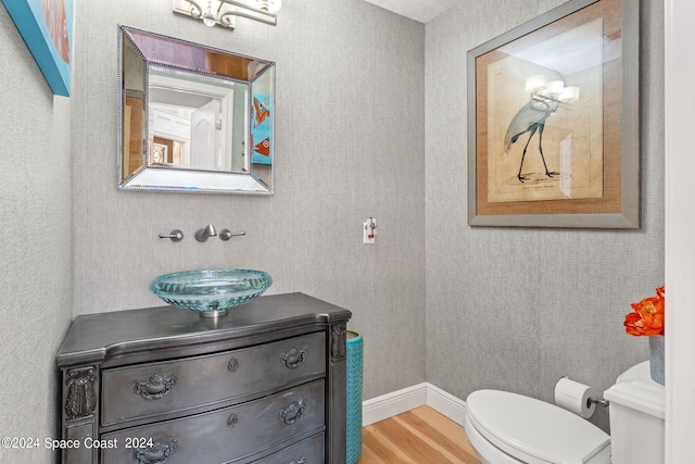 half bathroom featuring toilet, vanity, wood finished floors, baseboards, and wallpapered walls