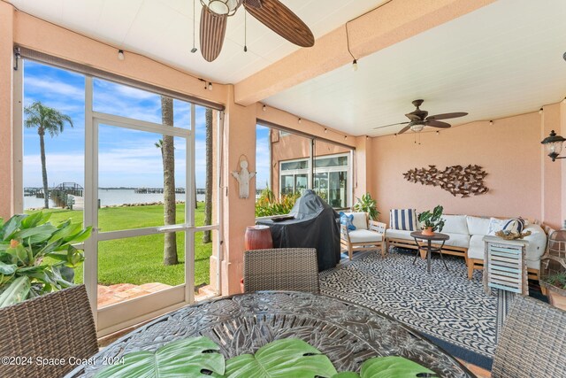 sunroom / solarium with a water view, beam ceiling, and ceiling fan