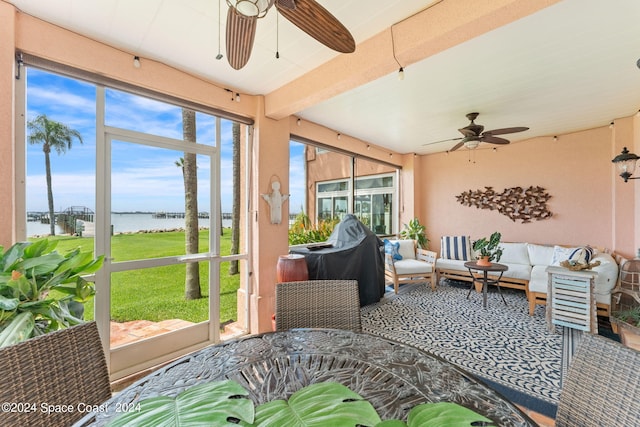 sunroom featuring a water view, ceiling fan, a wealth of natural light, and beamed ceiling