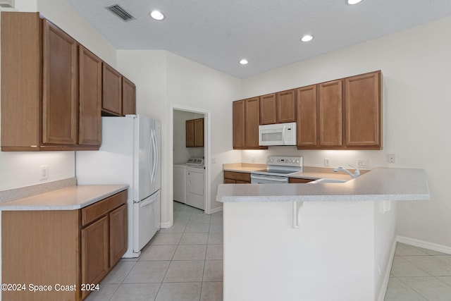 kitchen with light tile patterned floors, white appliances, sink, washing machine and clothes dryer, and a breakfast bar