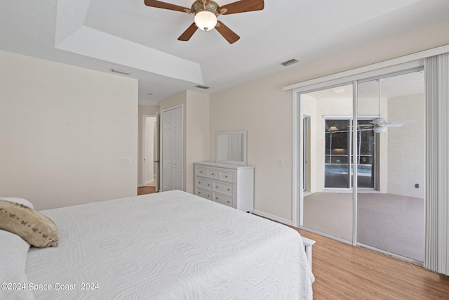 bedroom with light wood-type flooring, a tray ceiling, and ceiling fan