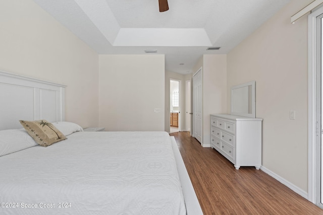 bedroom featuring ceiling fan, hardwood / wood-style flooring, a raised ceiling, and ensuite bath