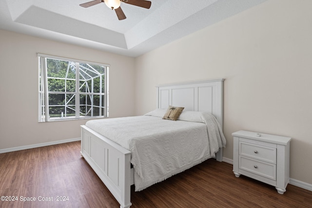 bedroom featuring a raised ceiling, dark hardwood / wood-style flooring, and ceiling fan