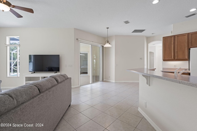 living room with a textured ceiling, ceiling fan, and light tile patterned flooring