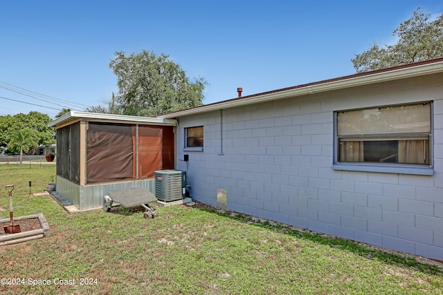 rear view of house with a sunroom, a lawn, and central AC