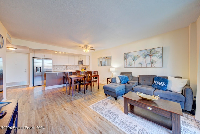 living room featuring ceiling fan, a textured ceiling, and light hardwood / wood-style flooring