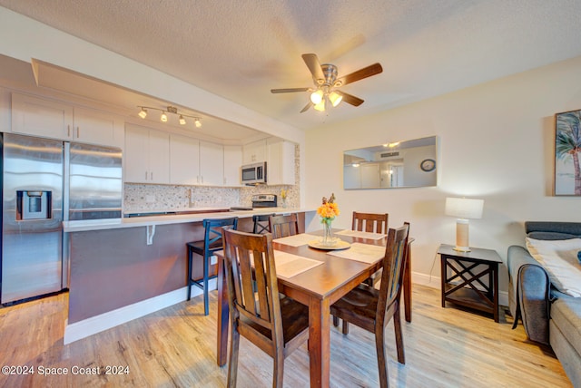 dining area featuring rail lighting, ceiling fan, a textured ceiling, and light hardwood / wood-style flooring