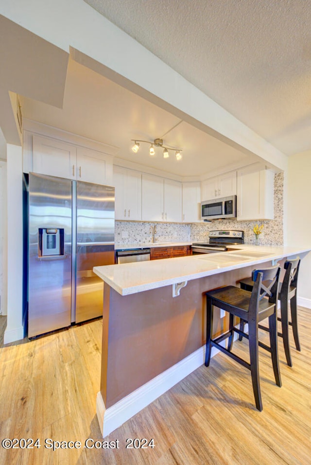 kitchen with stainless steel appliances, white cabinetry, track lighting, a kitchen bar, and decorative backsplash