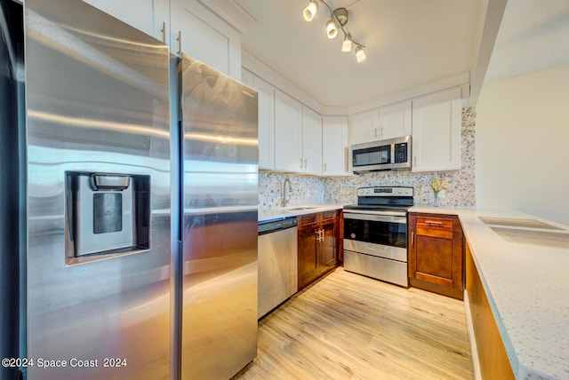 kitchen with light wood-type flooring, stainless steel appliances, white cabinetry, rail lighting, and decorative backsplash