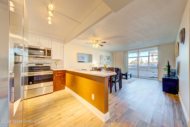 kitchen with appliances with stainless steel finishes, ceiling fan, kitchen peninsula, and light hardwood / wood-style flooring