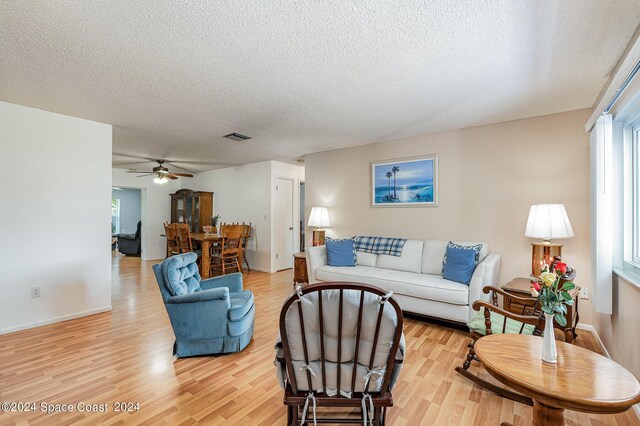 living room featuring light wood-type flooring, ceiling fan, and a textured ceiling