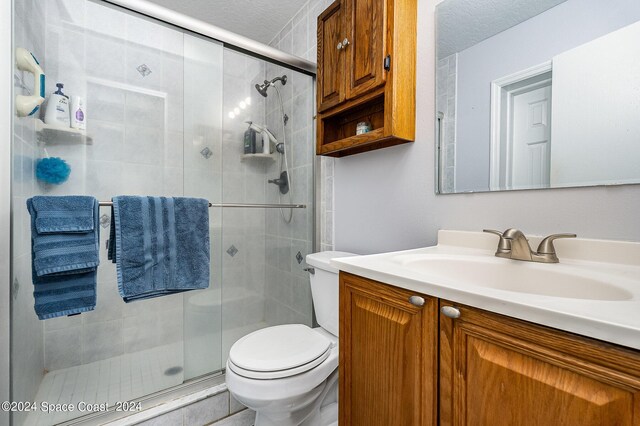 bathroom featuring vanity, toilet, a shower with shower door, and a textured ceiling