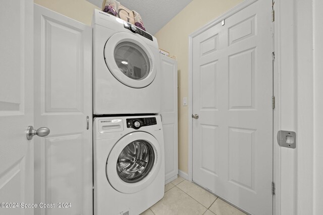 clothes washing area with a textured ceiling, stacked washer and clothes dryer, and light tile patterned flooring