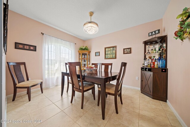 dining space with bar, light tile patterned floors, an inviting chandelier, and a textured ceiling