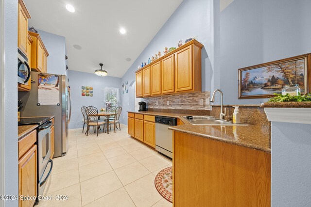 kitchen with dark stone countertops, stainless steel appliances, sink, vaulted ceiling, and light tile patterned flooring