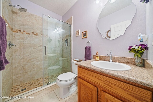 bathroom featuring tile patterned flooring, a shower with door, toilet, vanity, and a textured ceiling