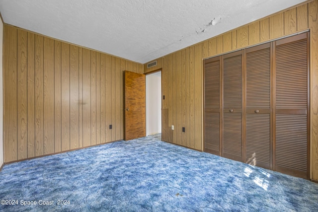 unfurnished bedroom featuring visible vents, wood walls, a textured ceiling, and carpet flooring