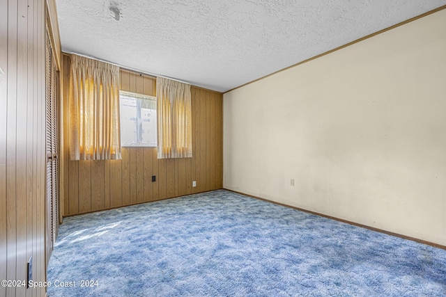 spare room with a textured ceiling, wooden walls, baseboards, and carpet flooring