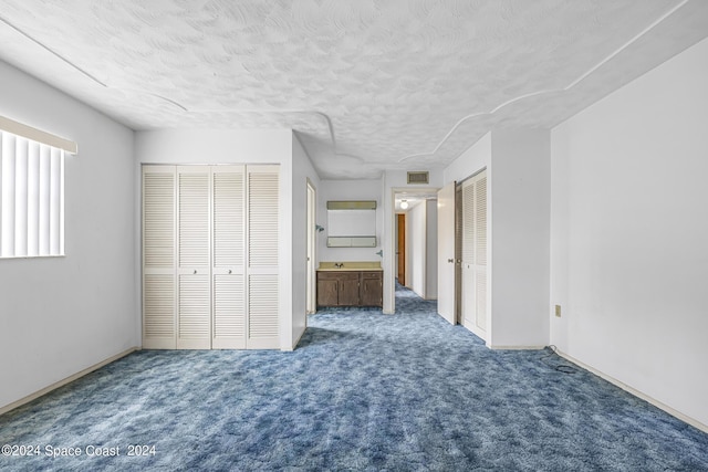 unfurnished bedroom featuring multiple closets, visible vents, a textured ceiling, and carpet flooring