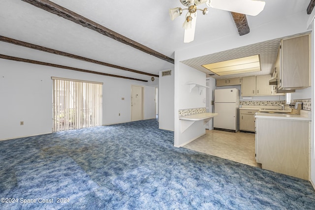 kitchen with a sink, open floor plan, light countertops, beam ceiling, and freestanding refrigerator