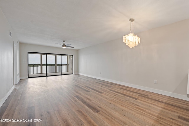 empty room featuring ceiling fan with notable chandelier and hardwood / wood-style flooring