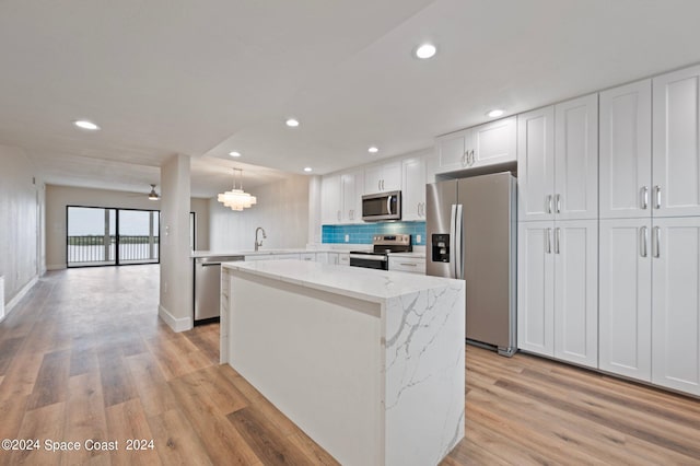 kitchen with light stone countertops, light hardwood / wood-style flooring, appliances with stainless steel finishes, kitchen peninsula, and white cabinetry