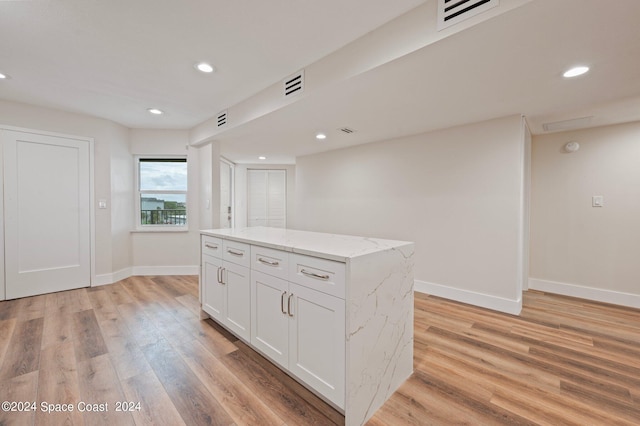 kitchen featuring light stone counters, a center island, white cabinets, and light hardwood / wood-style floors