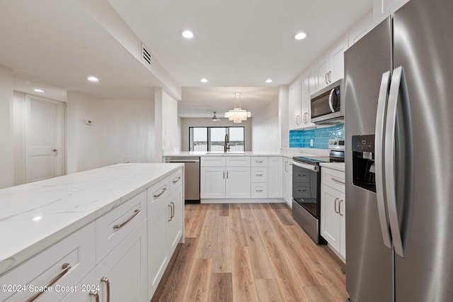 kitchen featuring light stone countertops, light hardwood / wood-style flooring, appliances with stainless steel finishes, kitchen peninsula, and white cabinets