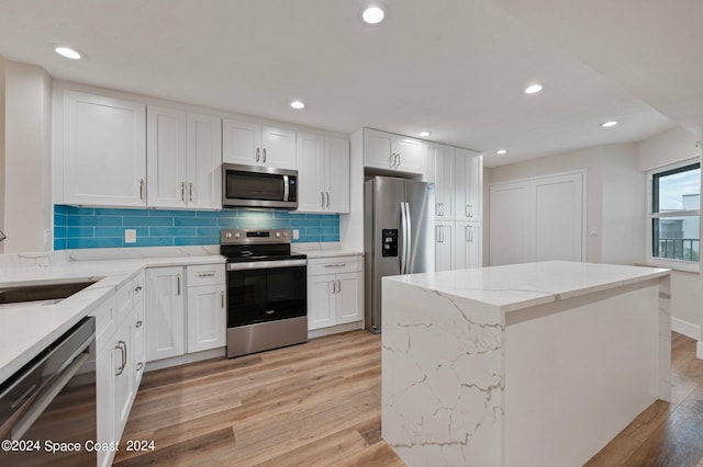 kitchen with light hardwood / wood-style flooring, appliances with stainless steel finishes, a center island, sink, and white cabinetry