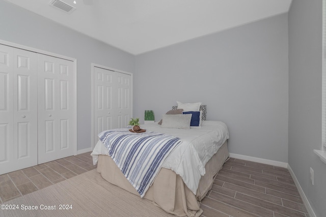 bedroom with baseboards, wood tiled floor, visible vents, and two closets