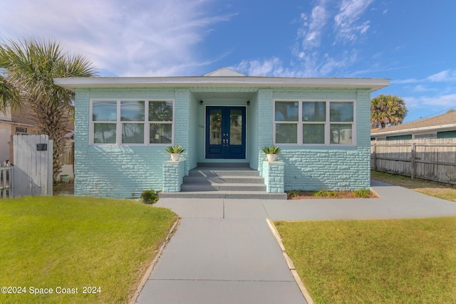 view of front facade with french doors, a front yard, fence, and brick siding