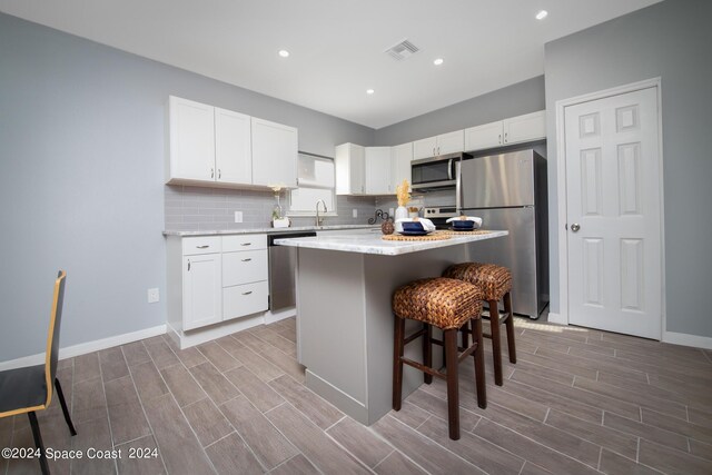 kitchen featuring a center island, appliances with stainless steel finishes, white cabinetry, and decorative backsplash