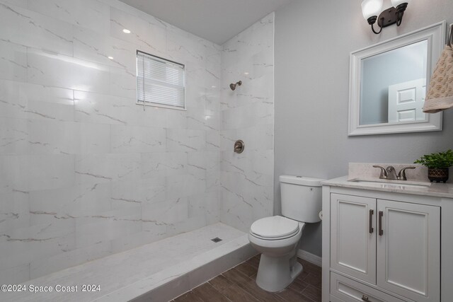 bathroom featuring wood-type flooring, toilet, a tile shower, and vanity