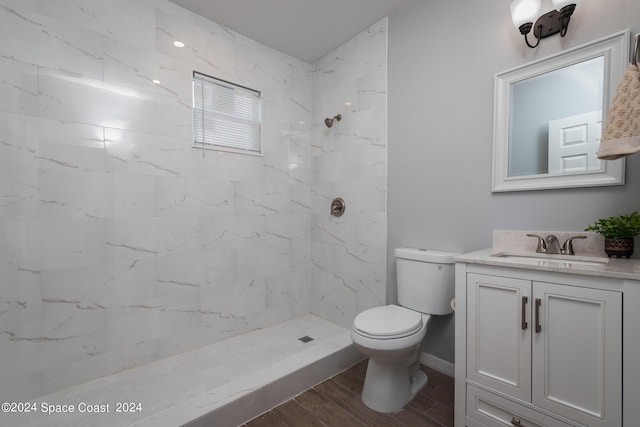 bathroom with toilet, wood tiled floor, a tile shower, vanity, and baseboards