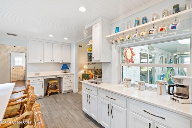 kitchen with built in desk, light stone countertops, sink, light wood-type flooring, and white cabinets