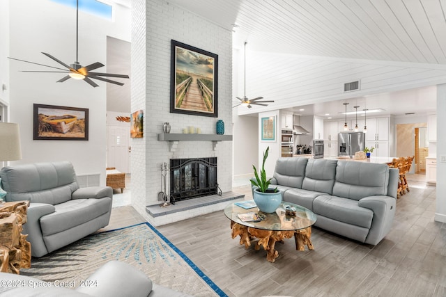 living room with light wood-type flooring, ceiling fan, high vaulted ceiling, and a brick fireplace