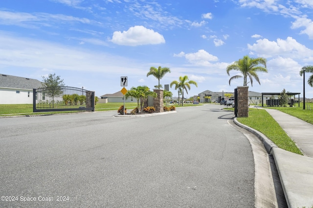 view of street featuring a gated entry, sidewalks, curbs, a residential view, and traffic signs